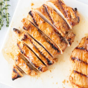 Top down shot of sliced grilled honey dijon chicken on a white cutting board.