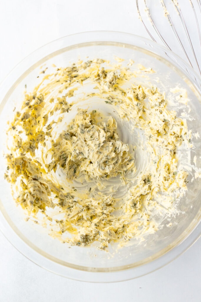 Whipped herb butter in a large clear bowl on a white background.