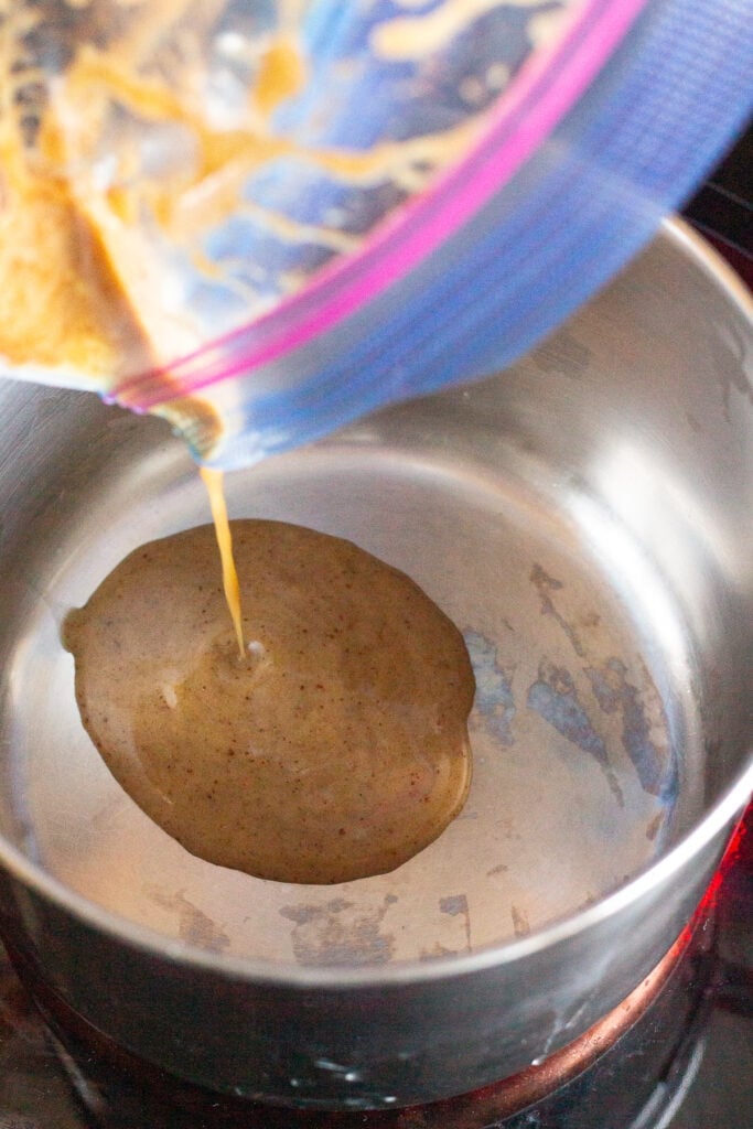 Used marinade being poured from a plastic ziploc bag into a small saucepan on the stove.