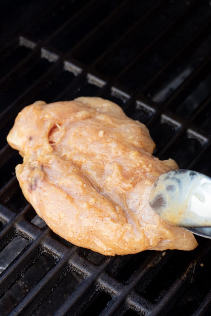 Placing raw marinated chicken breast on a hot grill with tongs.
