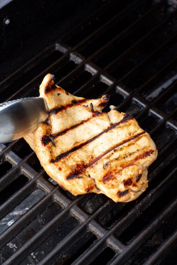 Flipping a grilled chicken breast over on a grill with metal tongs.