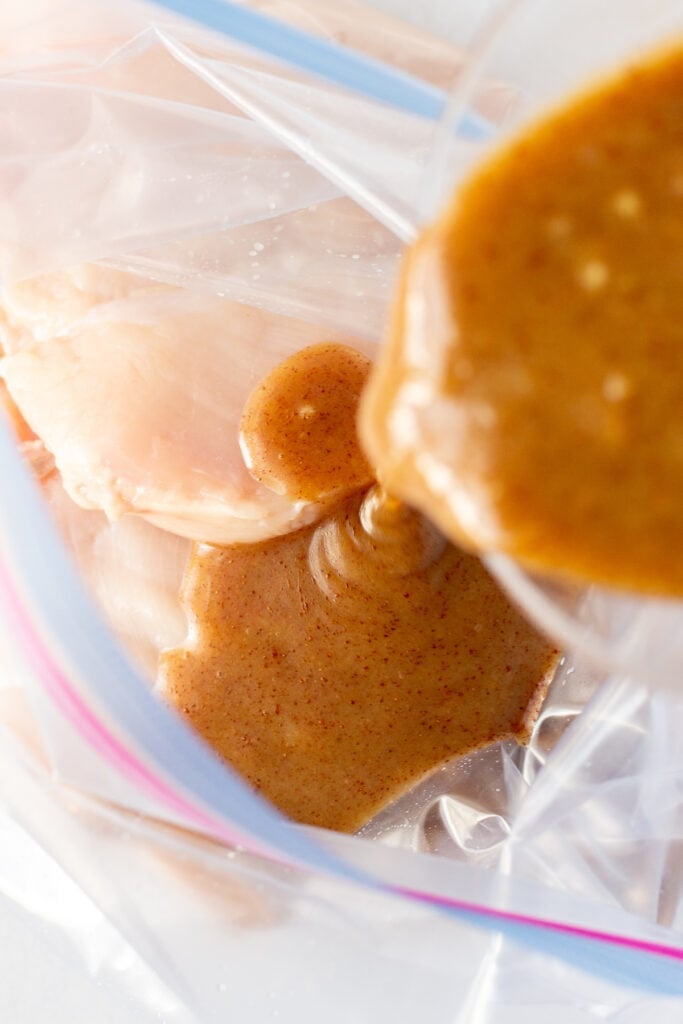 Pouring a brown honey mustard marinade over raw chicken breasts in a gallon sized ziploc plastic bag.