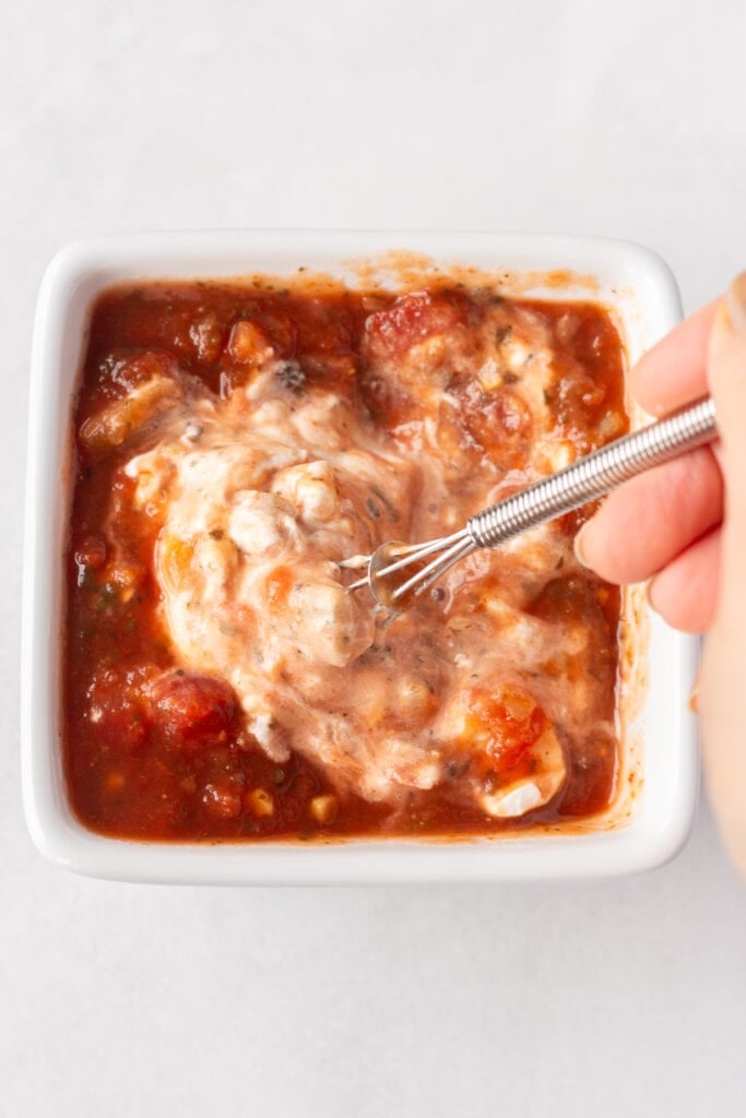 Sour cream and salsa being mixed together with a whisk in a white square dish.