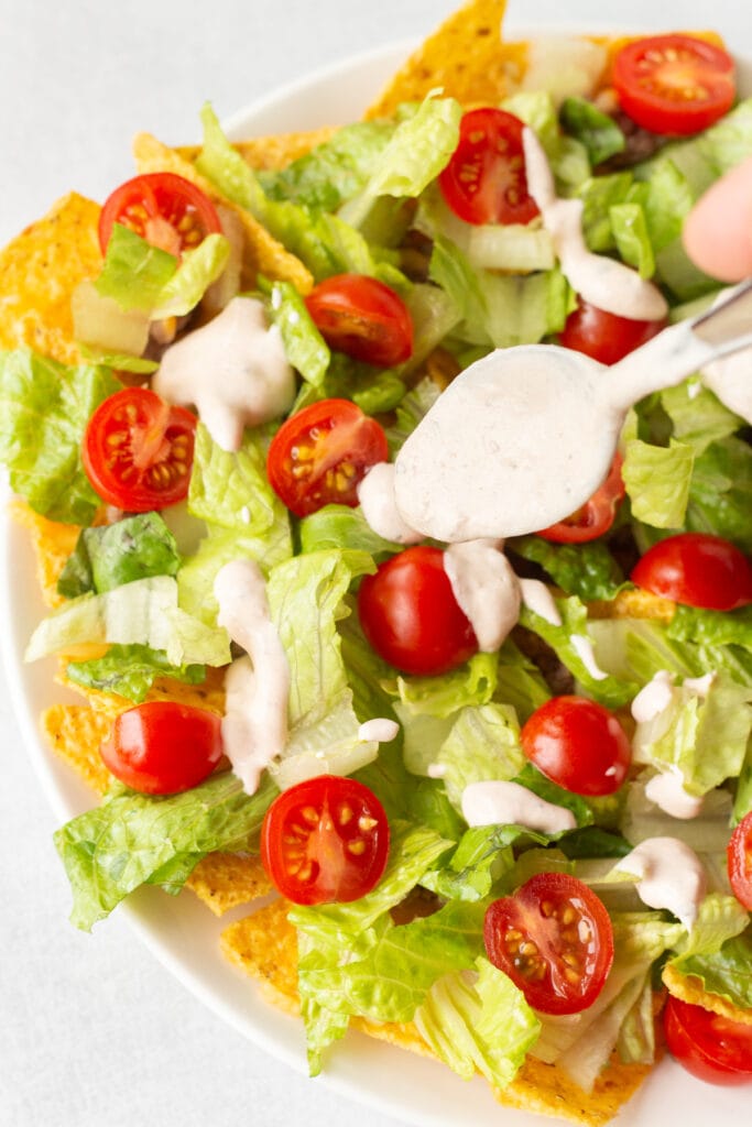 A spoon dripping salsa sour cream dressing onto a plate of nacho salad.