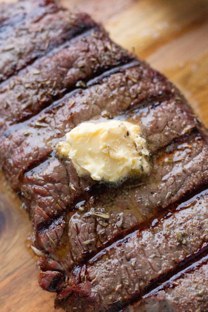 A grilled strip steak on a wood cutting board with a small slab of garlic butter melting on top of it.