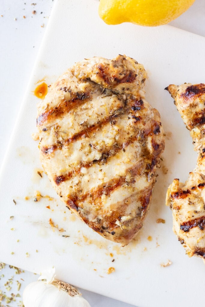 Top down shot of a grilled lemon herb chicken breast on a white cutting board.