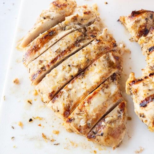 Top down shot of a grilled and sliced chicken breast on a white cutting board.