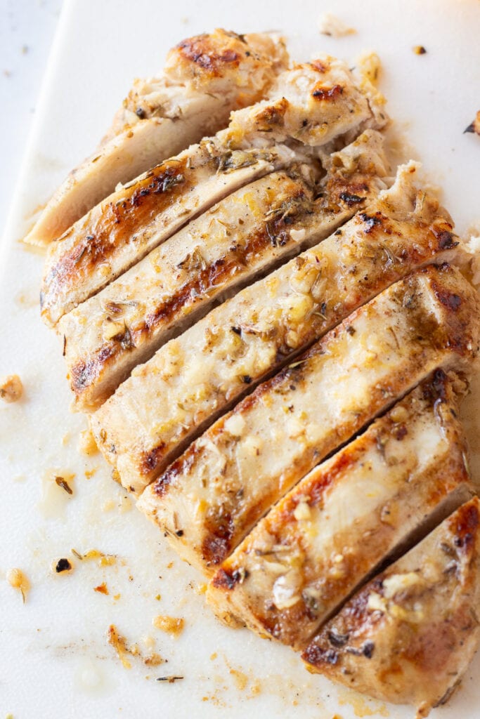 Close up of a grilled, lemon marinated chicken breast that's sliced on a white cutting board.
