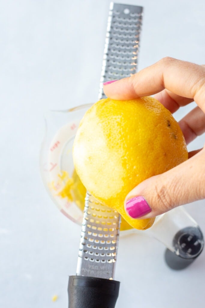 A lemon being zested with a microplane over a measuring cup.