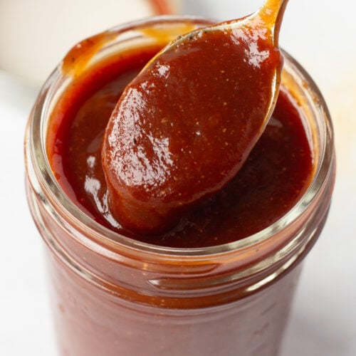Close up of apricot barbecue sauce in a small mason jar with a spoon dipping in it.