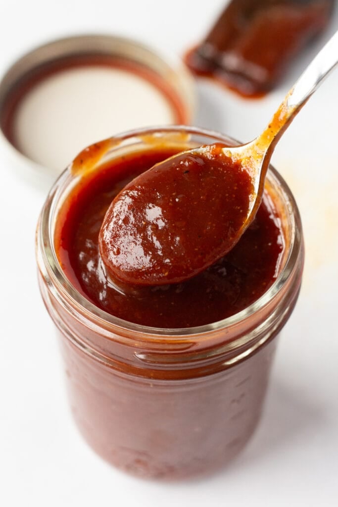Close up of apricot bbq sauce in a small mason jar with a spoon in it.