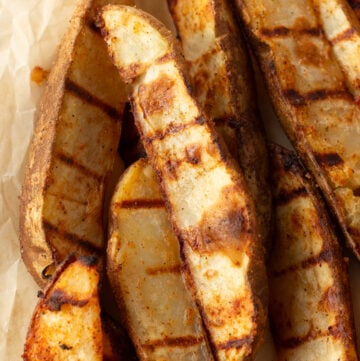Close up of grilled potato wedges on brown parchment paper.