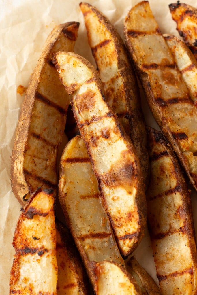 Close up of grilled potato wedges on brown parchment paper.