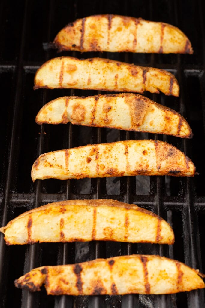 russet potato wedges being cooked on a grill.
