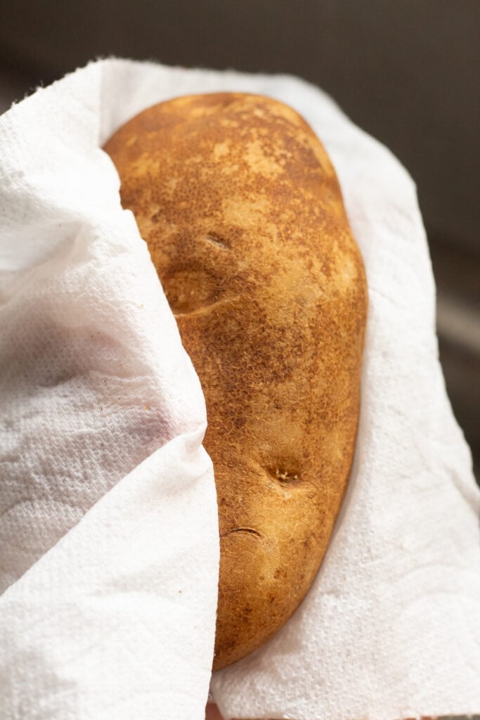 a washed russet potato being dried off with a paper towel.