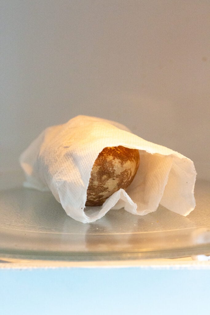 A russet potato wrapped in a damp paper towel in a microwave.
