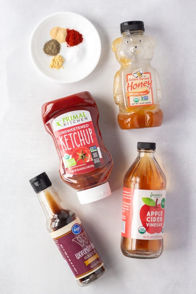 Top down shots of ingredients for honey bbq sauce on a white background, including ketchup, Worcestershire sauce, apple cider vinegar, honey, and spices in a small white plate.