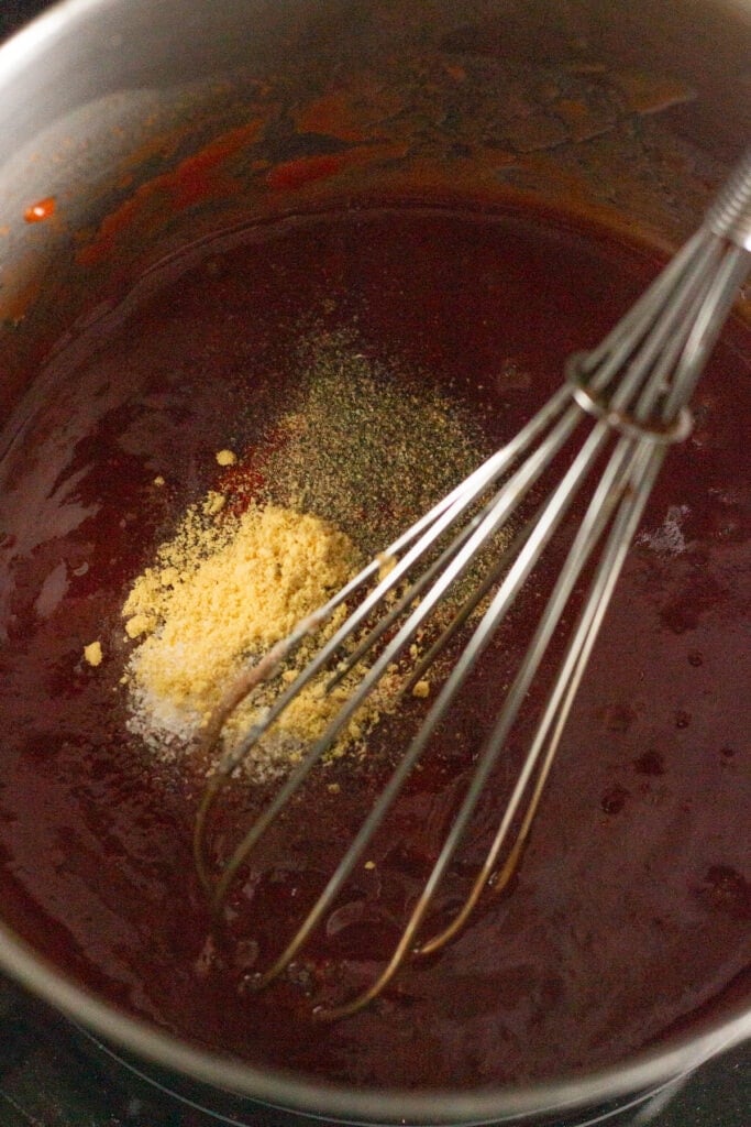 Close up of the inside of a sauce pan with a whisk in it and the makings of a bbq sauce, including some spices that haven't been mixed in yet.