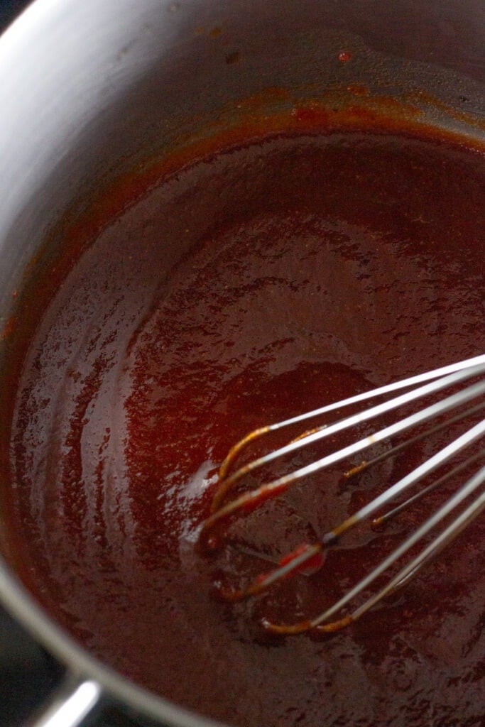 Close up of a whisk stirring bbq sauce in a small sauce pan.