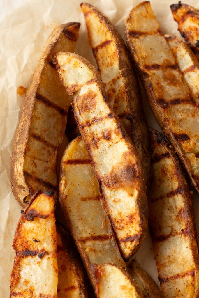 Close up of grilled potato wedges on some crinkled brown parchment paper.