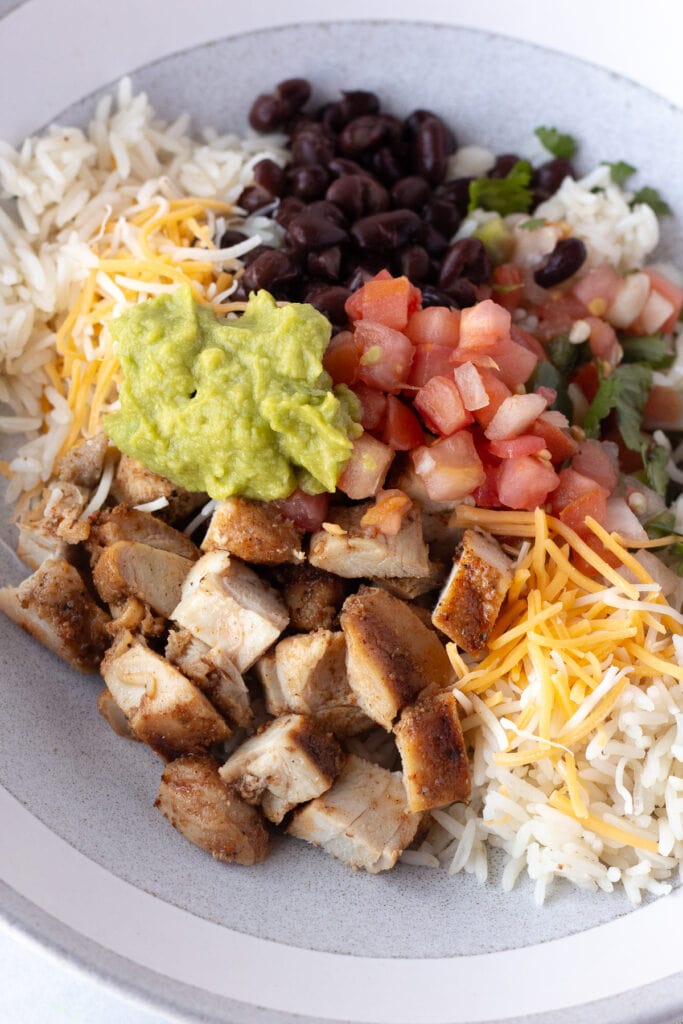 Close up of a grilled chicken burrito bowl with chopped chicken, white rice, guacamole, pico de gallo, black beans, and shredded cheese.