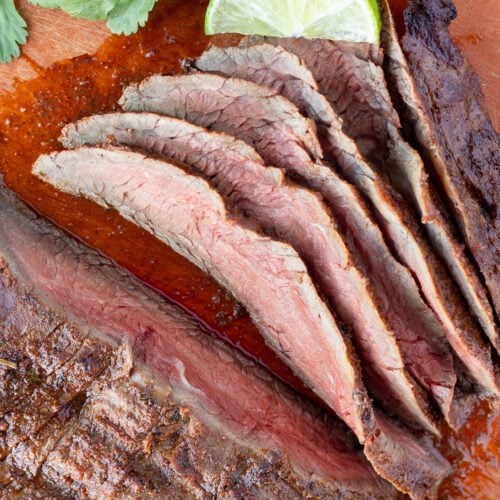 Close up of sliced chili lime flank steak on a cutting board with fresh cilantro and cut lime in the background.