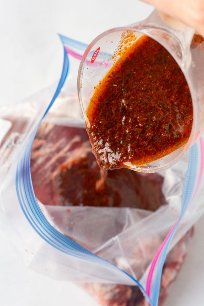 pouring a taco chili lime marinade onto raw flank steak in a ziploc plastic bag.