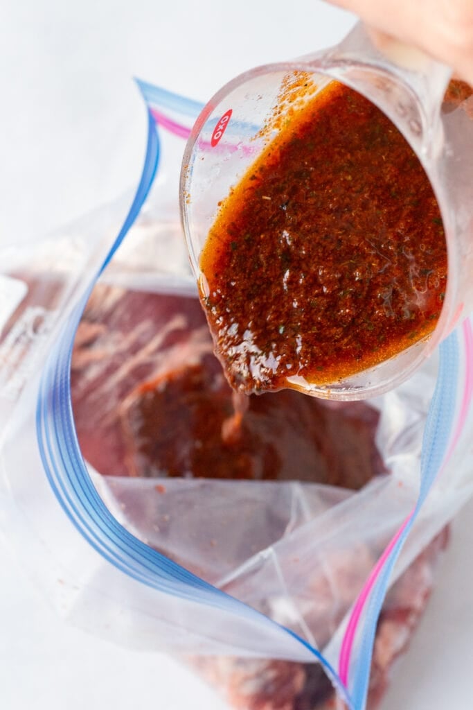 Pouring chili lime marinade into a gallon sized ziploc bag with a raw flank steak in it.
