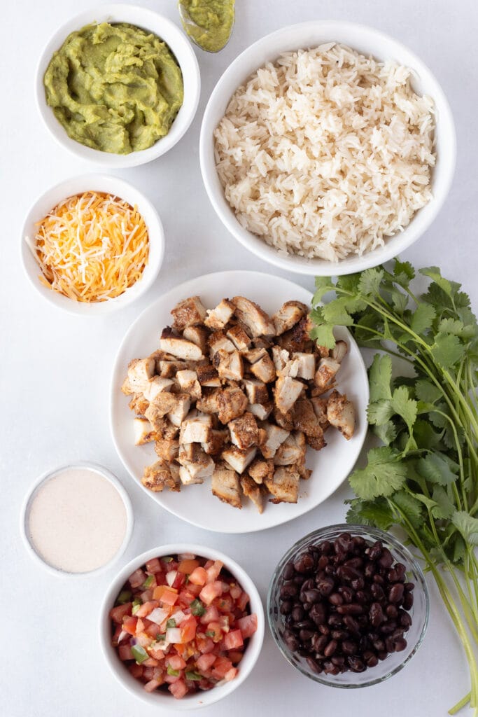 top down shot of ingredients for a grilled chicken burrito bowl on a light gray background.