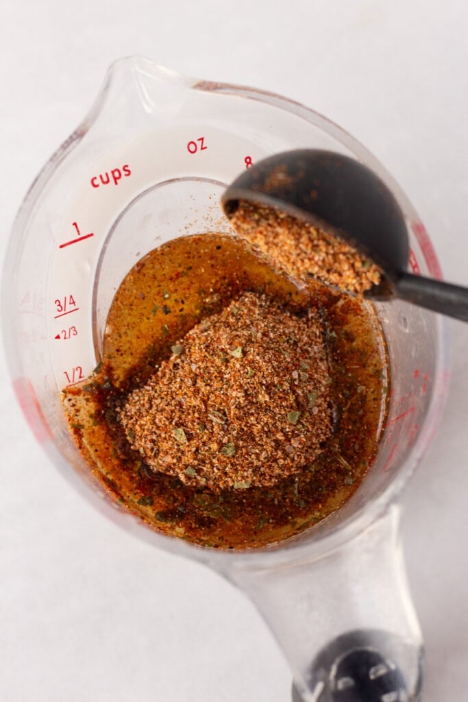 Close up of spices being poured into a liquid measuring cup of oil and lime juice.
