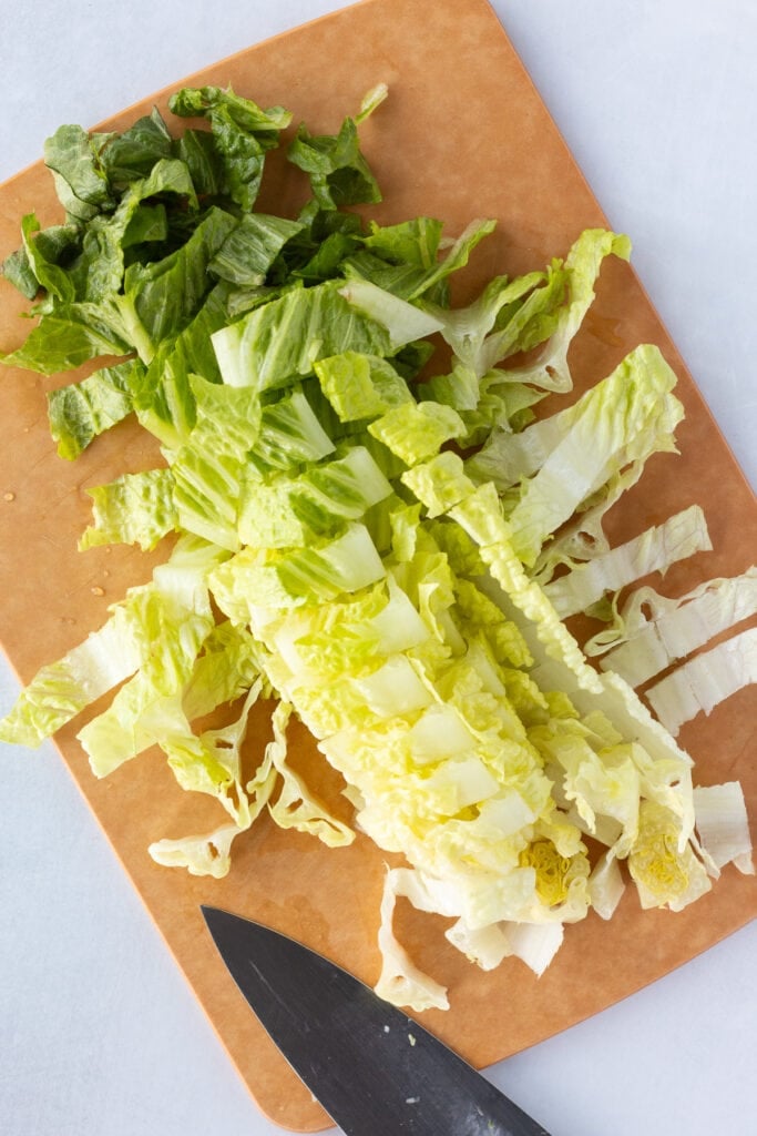 Top down shot of a cut up head of romaine lettuce on a brown cutting board.