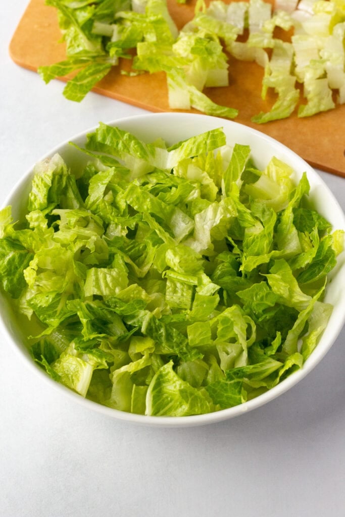 Close up of a low white bowl with chopped up romaine lettuce in it.