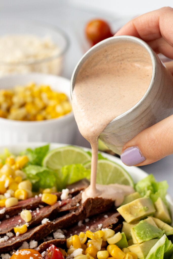 Close up of a hand pouring taco dressing over a steak salad.