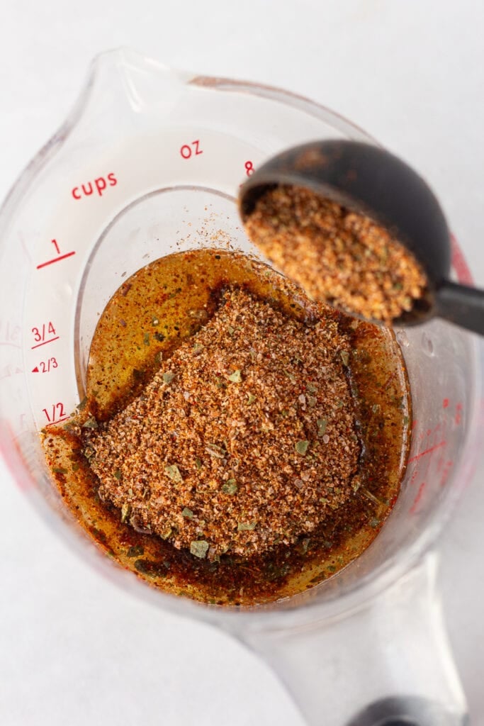 Close up of taco seasoning being dumped into a measuring cup that has oil and lime juice in it.