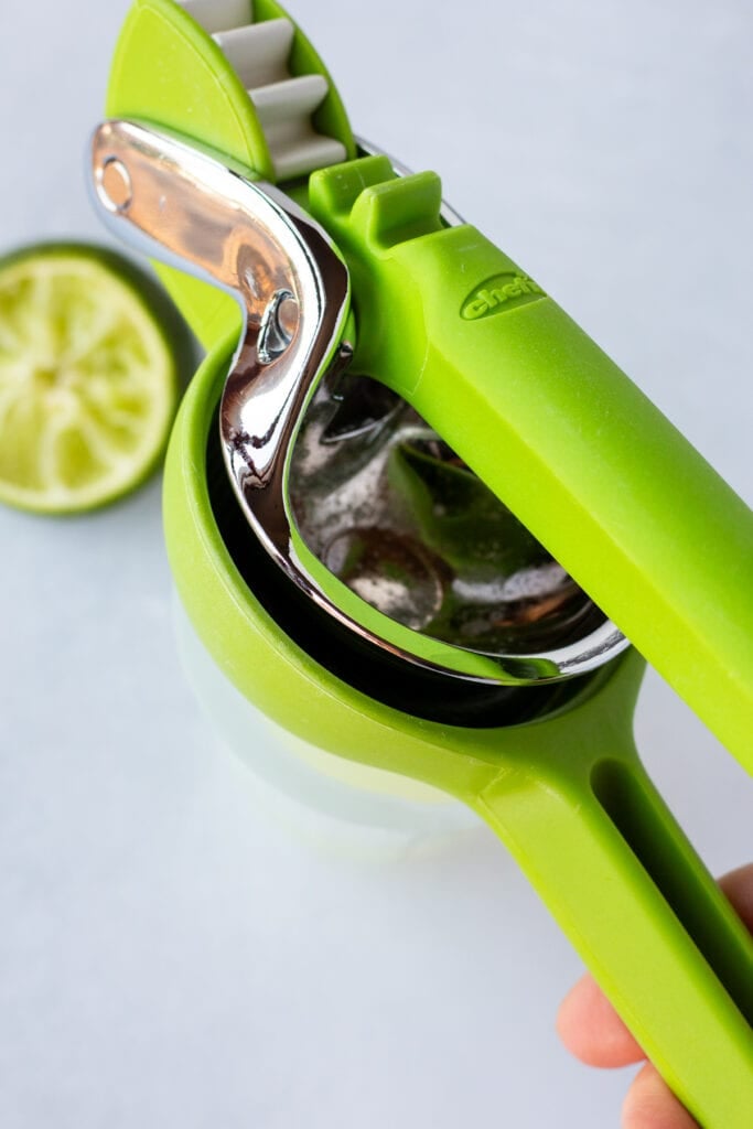 Close up of a lime being squeezed in a handheld green juicer.