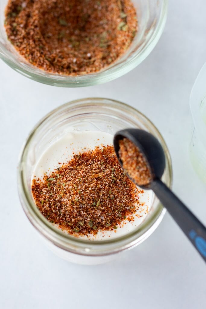 Pouring taco seasoning into a small mason jar with sour cream already in it.