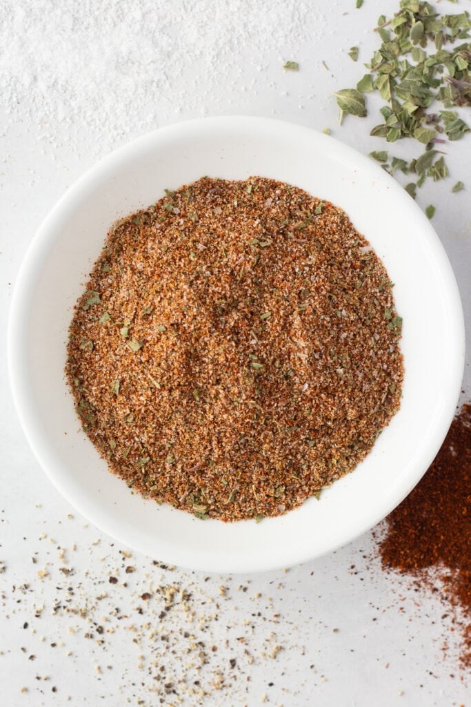 top down shot of taco seasoning blend in a small white bowl on a white background.