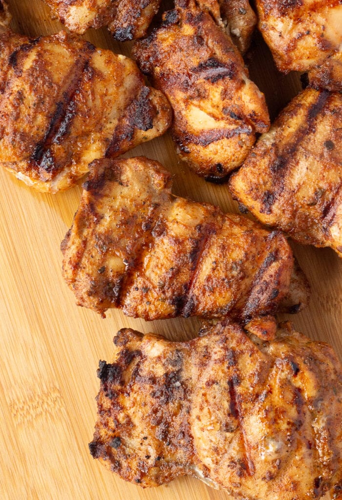 To down shot of grilled chicken thighs on a wood cutting board.