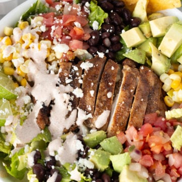 Top down shot of a grilled chicken taco salad in white low bowl with avocado, pico de gallo, black beans, corn, and lettuce in it.