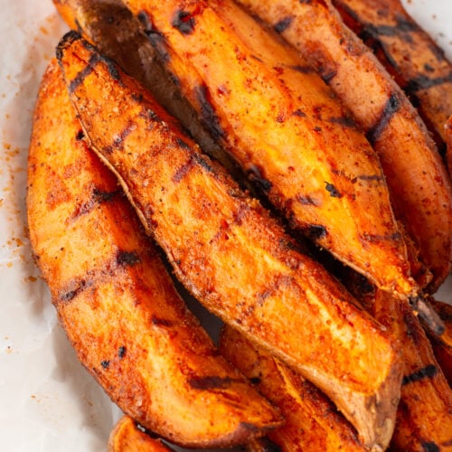 Close up of grilled sweet potato wedges on a white platter.