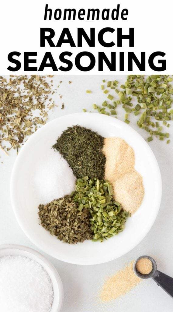 pin for ranch seasoning mix, showing the herbs and spices for the seasoning on a small white plate, with other herbs sprinkled around it.