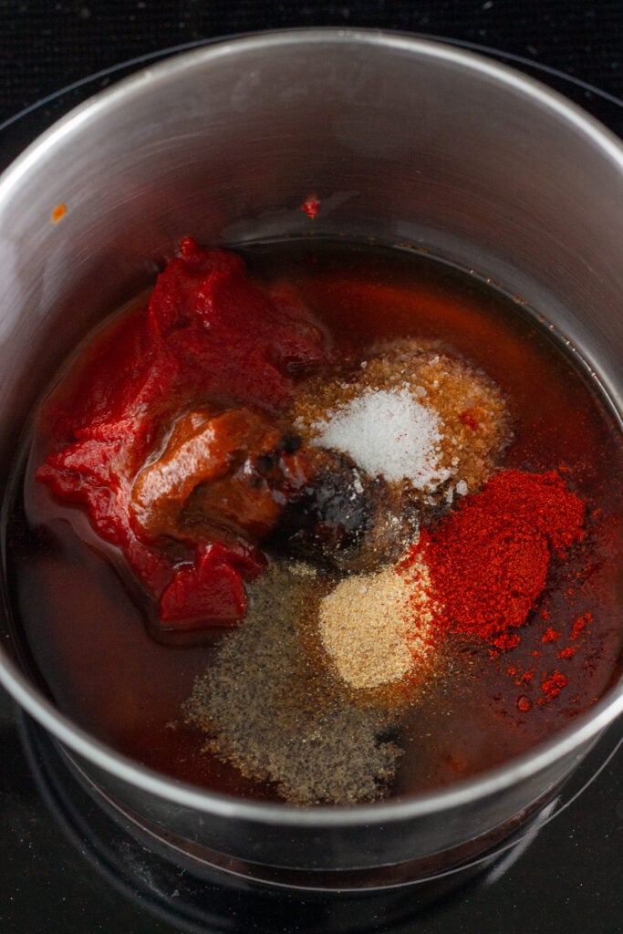 Zoomed in shot of ingredients in a saucepan, including tomato paste, peppers, maple syrup, and spices.