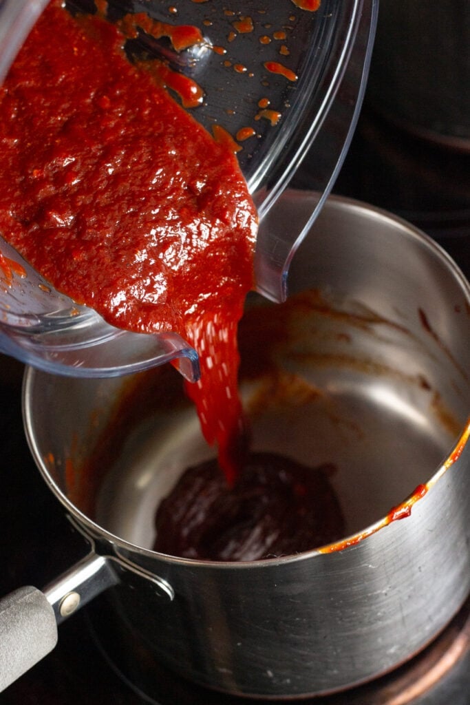 Close up of bbq sauce being poured from a blender container back into a sauce pan on the stove top.