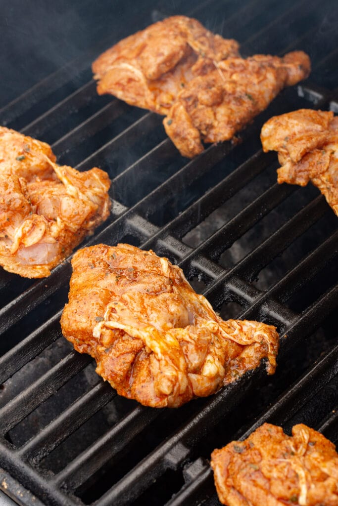 Marinated boneless skinless chicken thighs cooking on a hot gas grill.