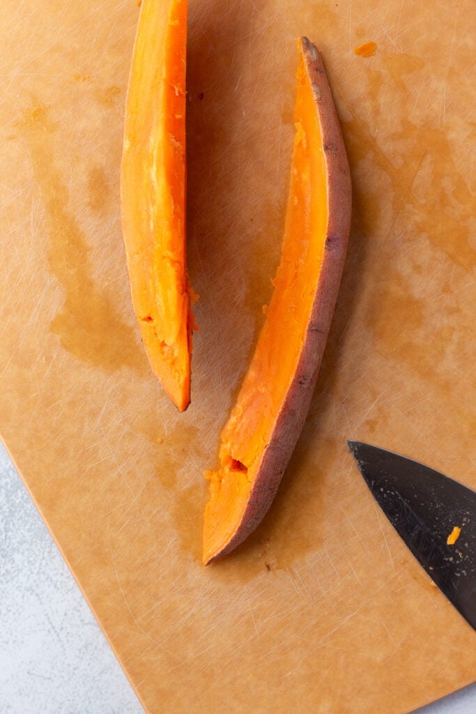 Top down shot of cut sweet potato wedges that have started to break, laying on a cutting board next to a knife.