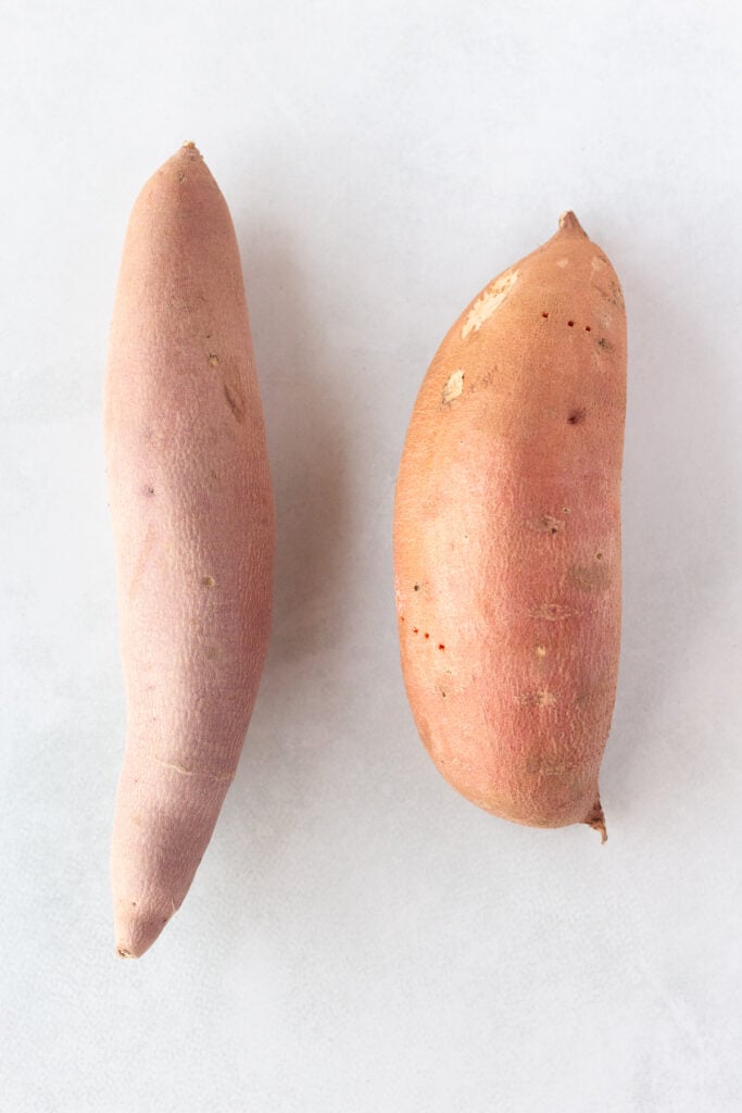 Top down shot of two sweet potatoes of different sizes on a light gray background.
