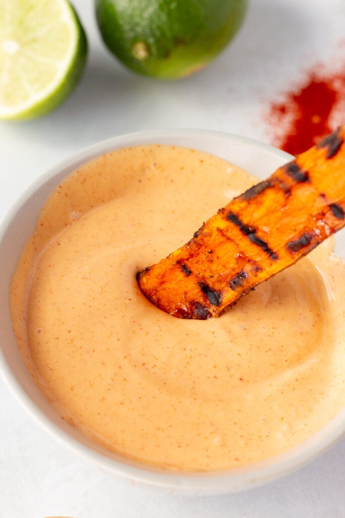 Close up of a grilled sweet potato wedge being dipped in a bowl of smoky mayo sauce.