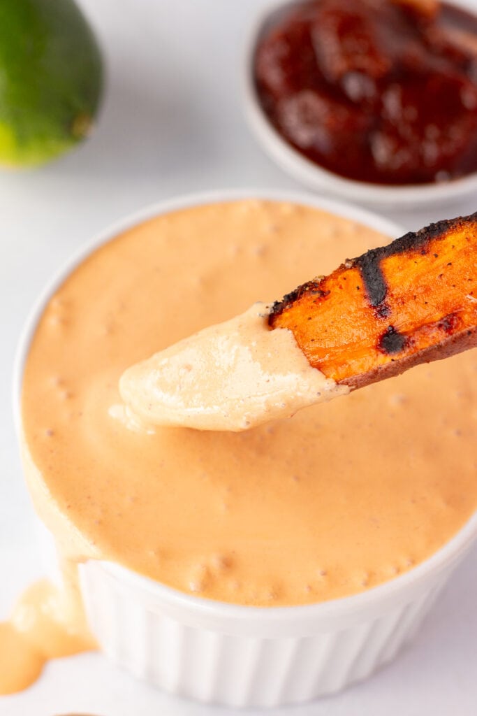 Close up of a grilled sweet potato wedge being dipped into a small white bowl with chipotle lime sauce in it.