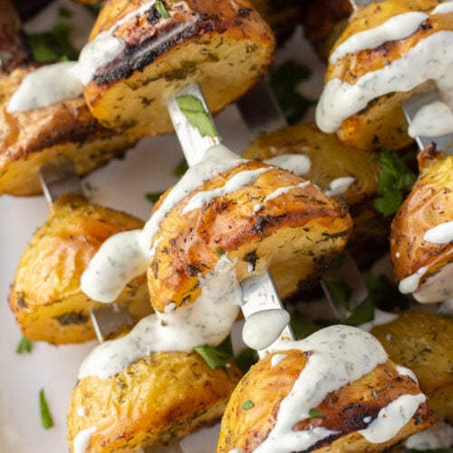 Close up of grilled ranch potatoes on metal skewers drizzled with ranch dressing.