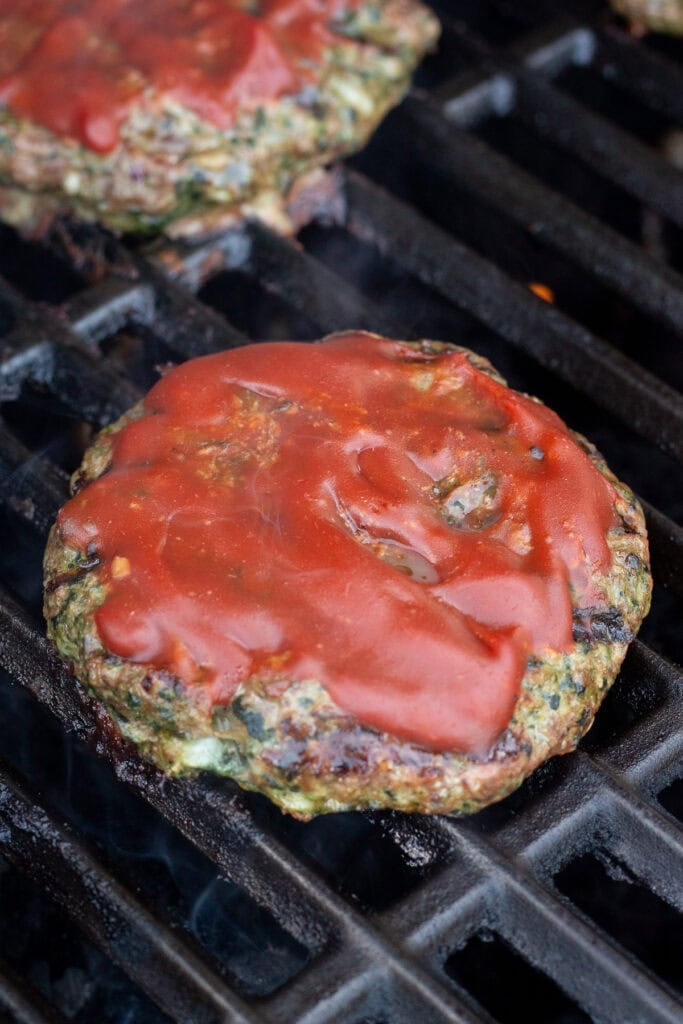 Close up of a meatloaf burger covered in ketchup on a grill.